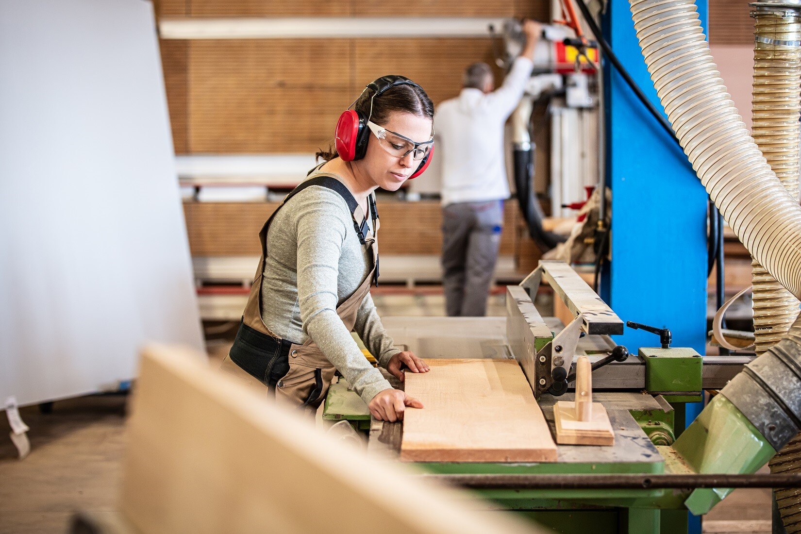 Tischlerin mit Gehörschutz und Schutzbrille arbeitet mit Holz an einer Werkbank