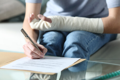 Mensch mit verbundenem linken Arm und Stift in rechter Hand.